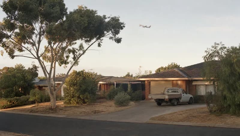 Quiet Perth suburban street at dawn with a plane climbing in the distance